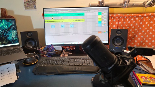 Computer screen showing audio recording software. There is a microphone in front of the screen, speakers to the side, and an orange curtain with white polka dots behind the screen.