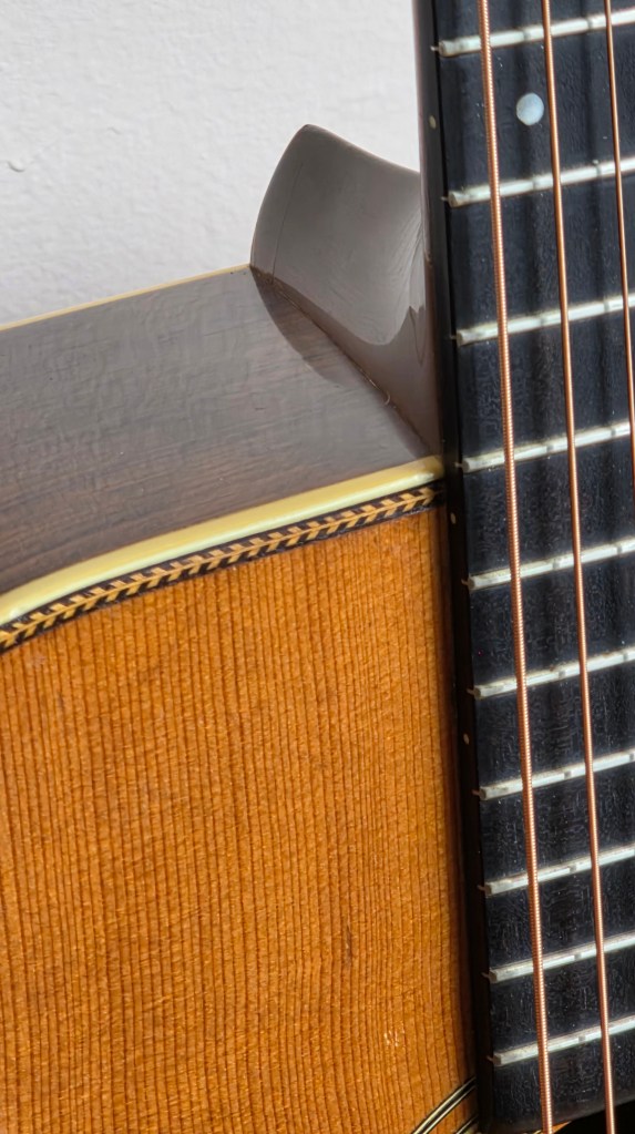 Close up of guitar fretboard where the neck joins the body, showing the heal attachment area, and herringbone trim on the top